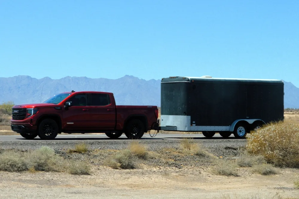 A red GMC Sierra pickup truck tows a black enclosed cargo trailer on a rural desert highway