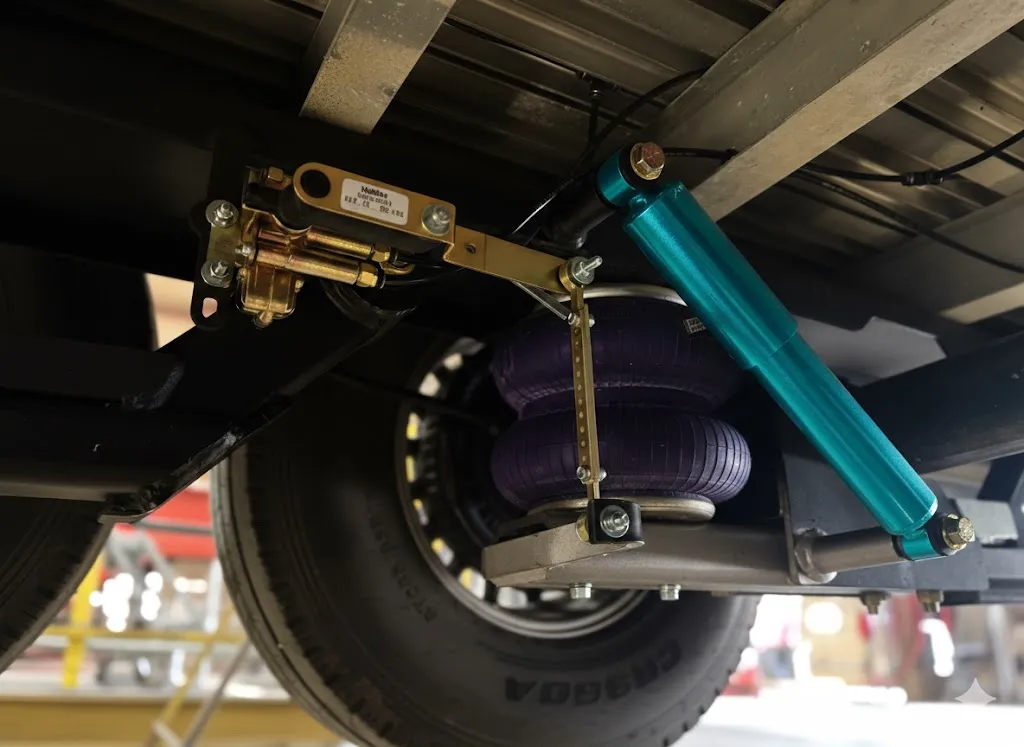 Close-up view of a trailer's torsion axle air suspension system featuring a teal shock absorber and purple air springs mounted under the chassis