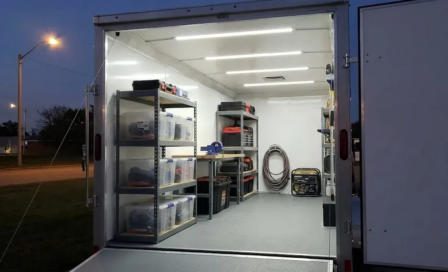 Well-lit enclosed trailer interior with shelves and organized tools.